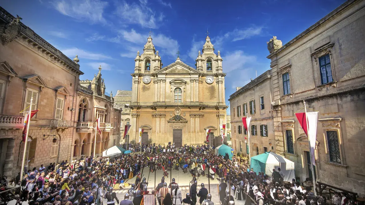 Tłum ludzi w historycznych strojach zgromadzony na placu przed katedrą w Mdina, Malta.