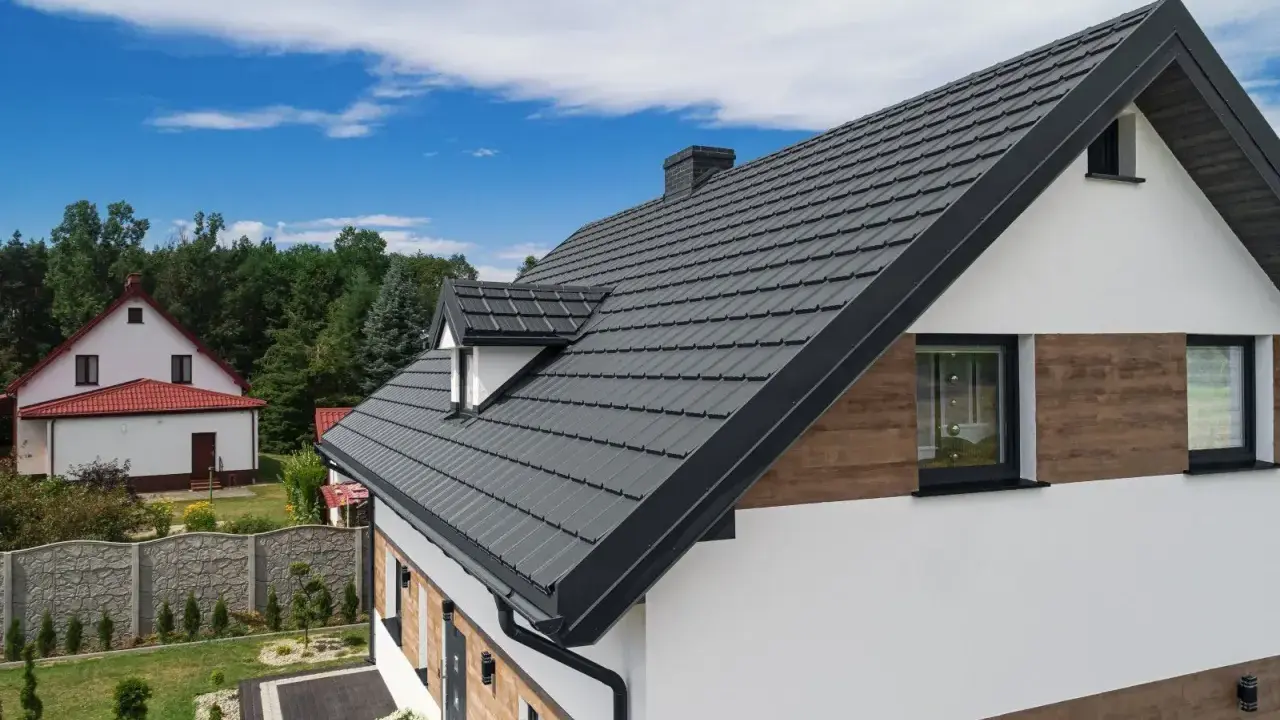 Nowoczesny dom z antracytową elewacją i dachówką, otoczony zielenią i błękitnym niebem.