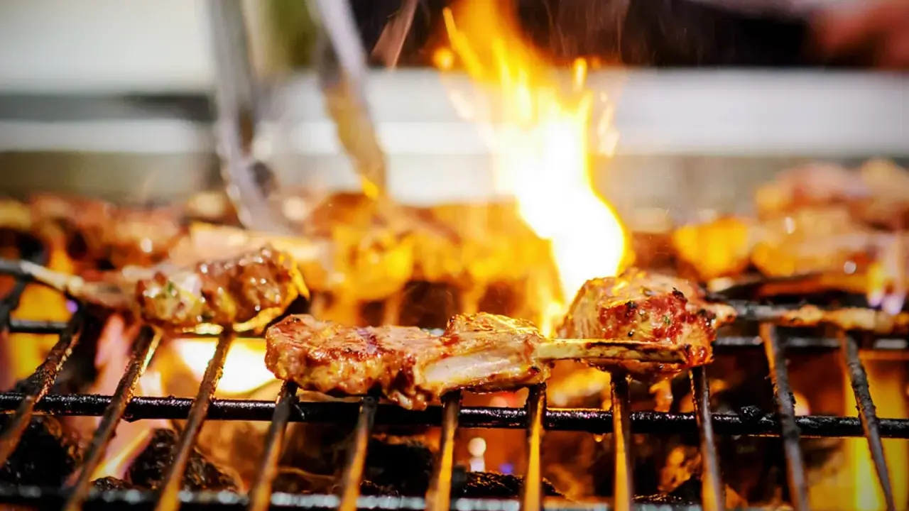 Marinierte Lammkoteletts brutzeln auf dem Grill. Flammen züngeln über dem Fleisch, das perfekt gegrillt wird.