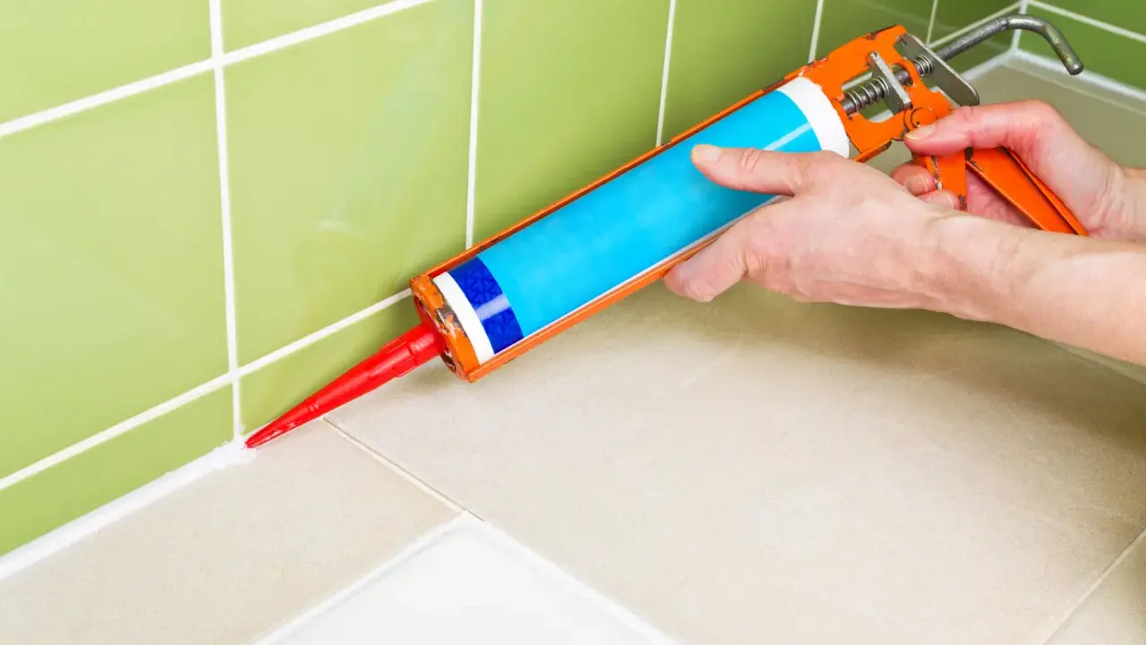 Application de silicone pour maçonnerie sur le joint entre le carrelage mural vert et le plan de travail beige.