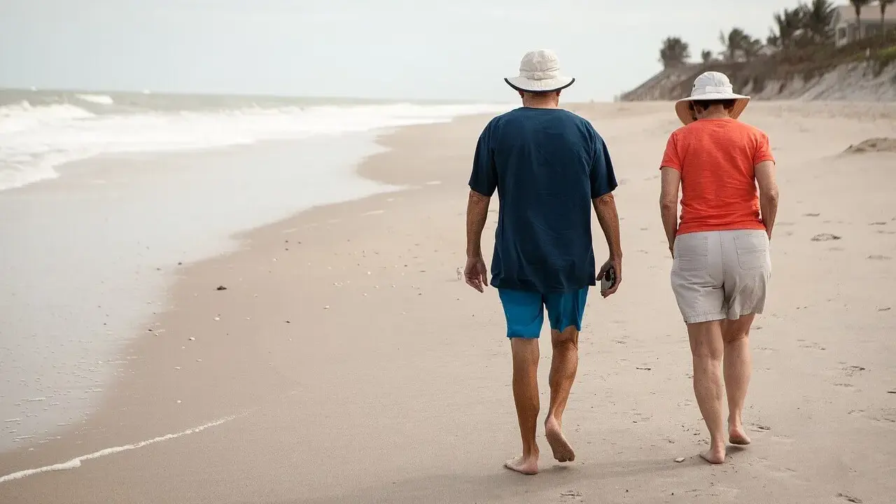 Spacerem po plaży idą emeryci. Słońce, morze i piasek tworzą idealne tło dla ich wspólnego wypoczynku.