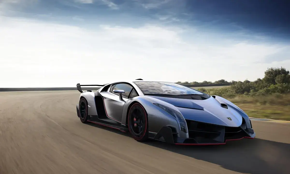 Silberner Lamborghini Veneno Coupé rast auf einer Rennstrecke, die roten Akzente leuchten.