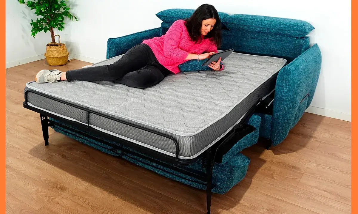 Mujer relajada en un sofá cama abierto, usando su tablet. Los sofabeds son perfectos para ahorrar espacio.