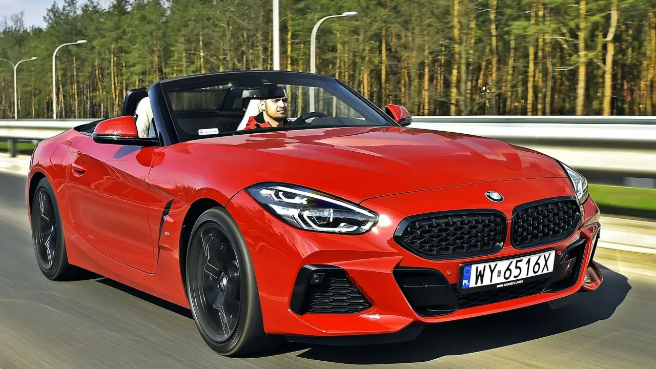 Czerwone z4 bmw z opuszczonym dachem pędzi po drodze, kierowca w czapce z daszkiem cieszy się jazdą.