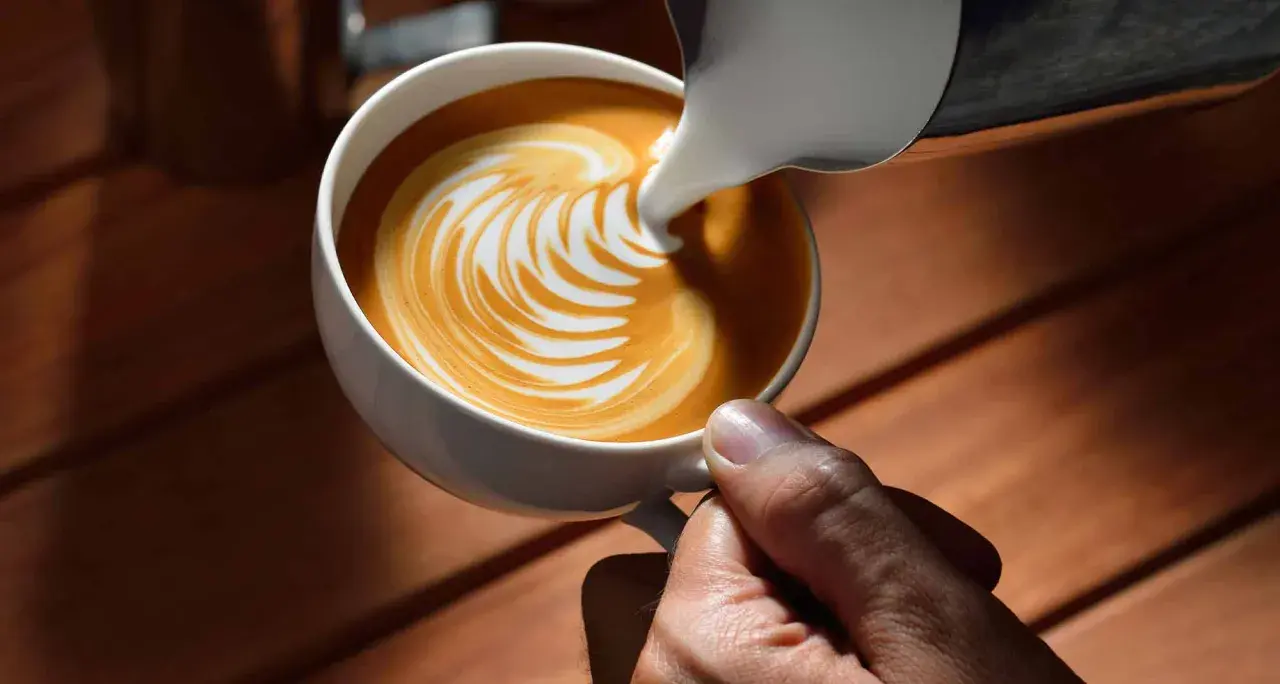 Barista gießt Milch in Kaffee für Latte Art. Der Unterschied zwischen Milchsorten beeinflusst das Ergebnis.