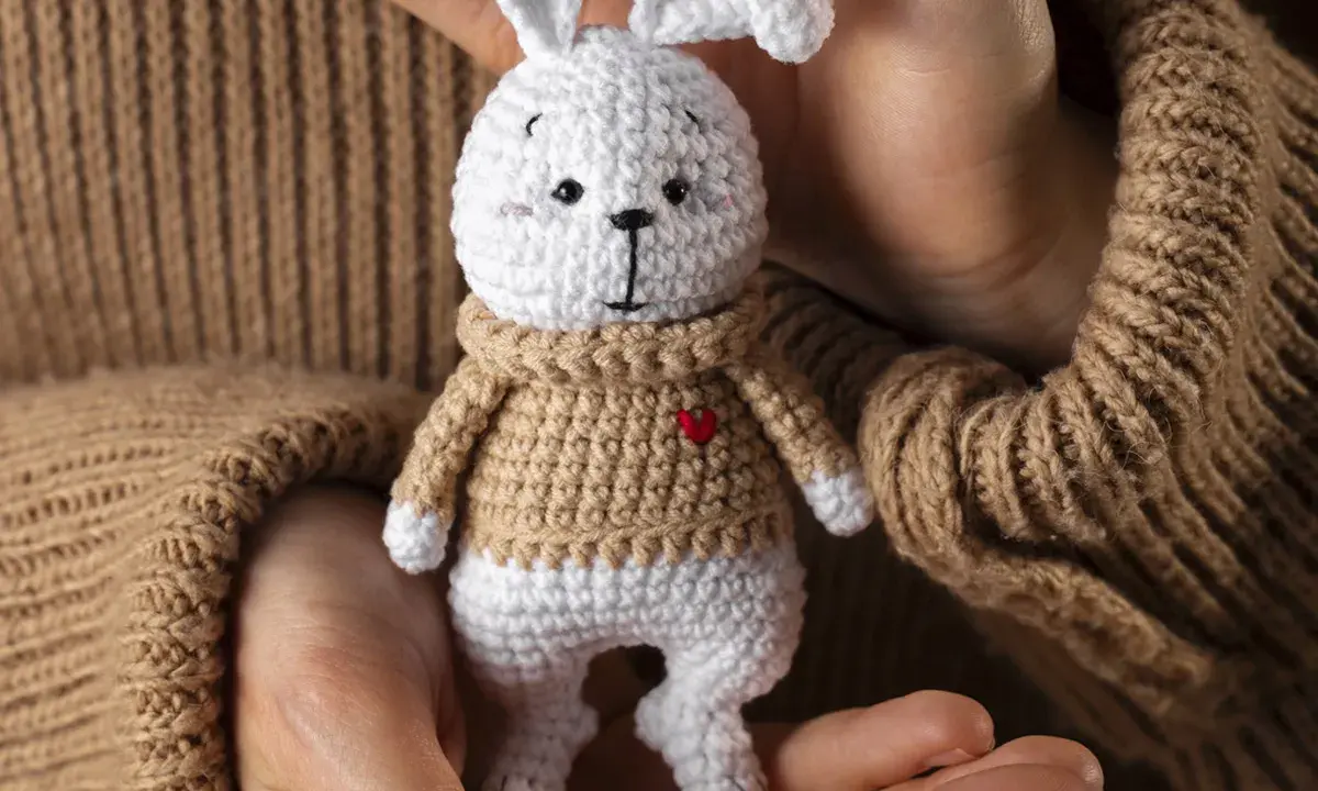 Un tierno conejito blanco con suéter tejido, parte de una colección de amigurumis originales, sostenido entre manos.