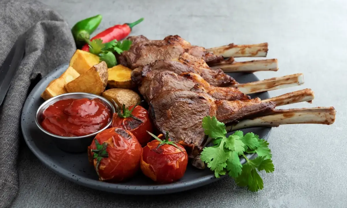 A perfectly grilled comber jagnięcy, served with roasted tomatoes, potato wedges, chili peppers, and a side of ketchup.