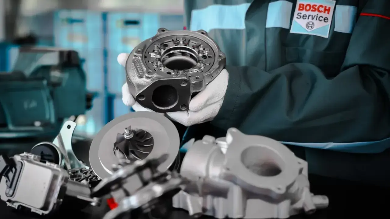 Mechanik w rękawiczkach prezentuje turbosprężarkę do silnika diesla, obok leżą jej części.