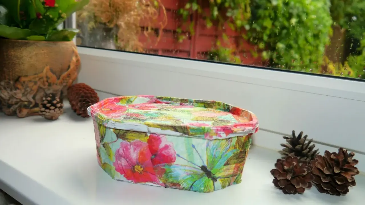 Uroczy koszyczek z motywem kwiatów i motyli, wykonany techniką decoupage na plastiku. Idealny do przechowywania drobiazgów.