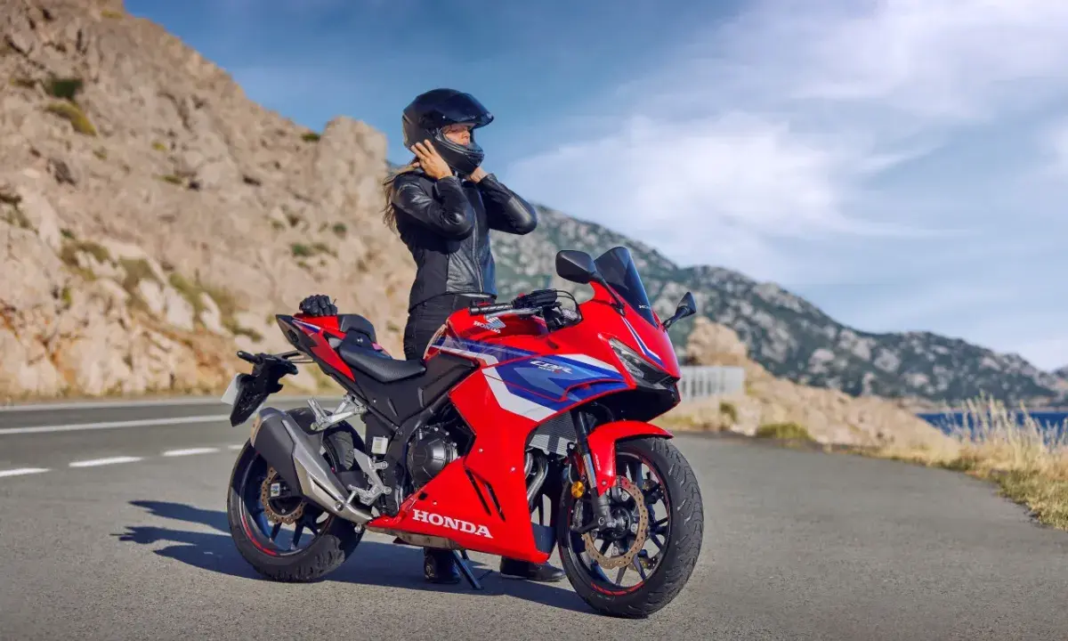 Kobieta w kasku i skórzanej kurtce przy czerwonym motocyklu Honda. Widok na góry i morze. Idealny na najszybsze motocykle na A2.