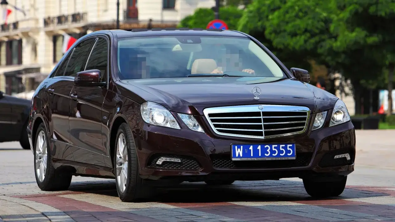 Ciemnobrązowy Mercedes z tablicami dyplomatycznymi W 113555, jadący po ulicy.
