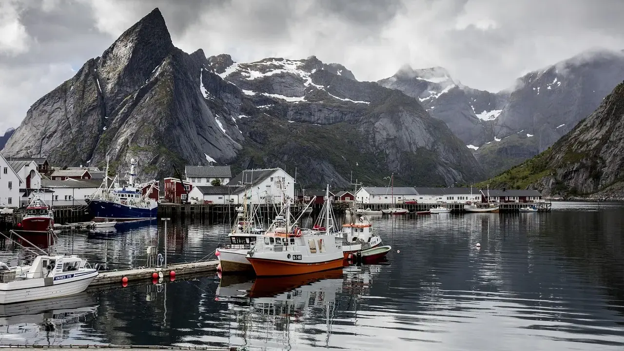 Port de pêche norvégien avec des montagnes imposantes en arrière-plan. Des bateaux de pêche sont amarrés, offrant un mouillage bateau gratuit dans ce paysage pittoresque.