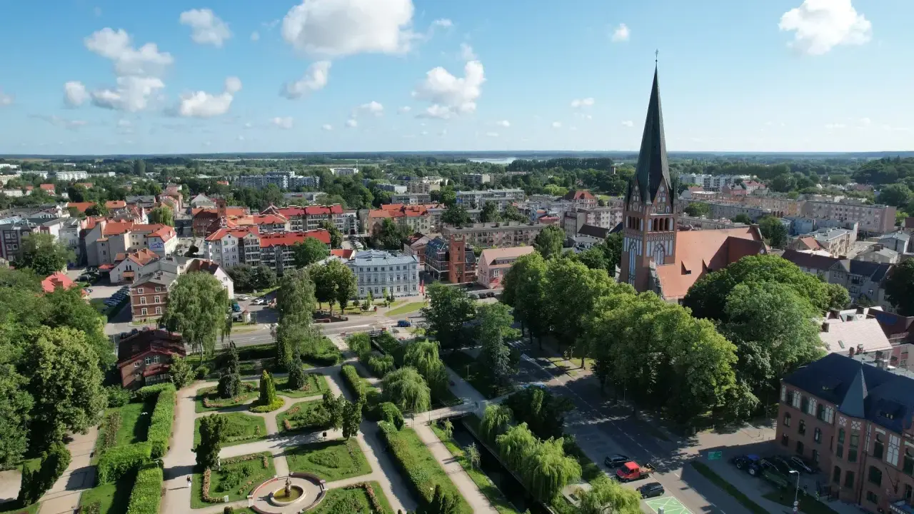 Widok z lotu ptaka na Szczecinek. Widać park miejski z fontanną, kościół z wieżą i zabudowania. To piękne **szczecinek atrakcje** turystyczne.