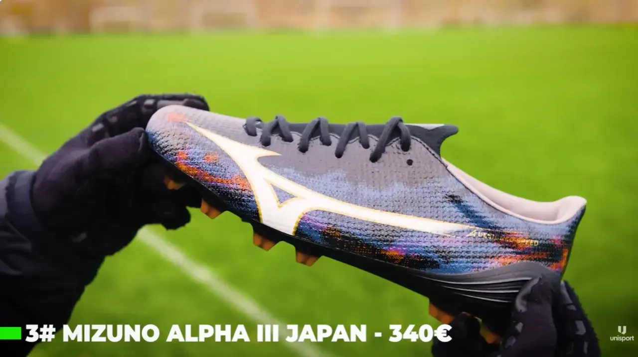 Ręce w rękawiczkach trzymają kolorowe korki Mizuno Alpha III Japan, które mogą być najlepszymi korkami na świecie.