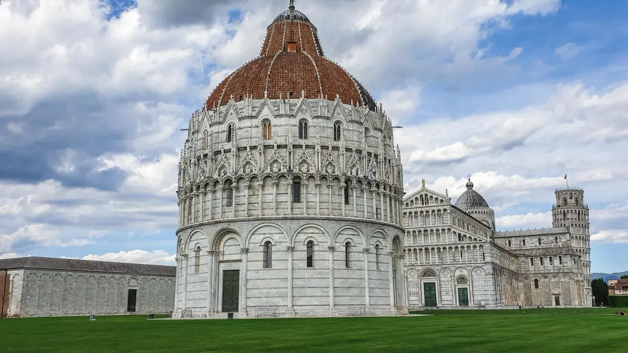 Il Battistero, il Duomo e la Torre Pendente: ecco cosa vedere a Pisa in un giorno, un'iconica piazza con un prato verde e cielo nuvoloso.