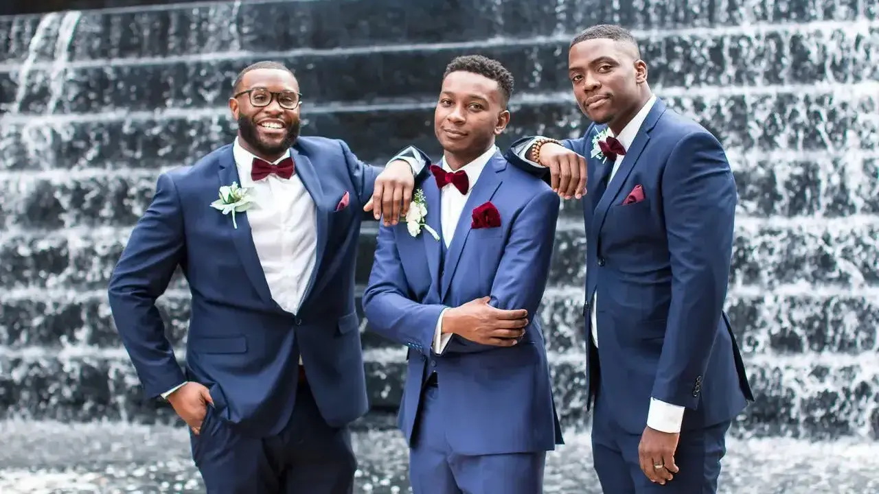 Three groomsmen in navy blue suits with burgundy bow ties and boutonnieres. A stylish guide on how to wear a blue suit for any occasion.