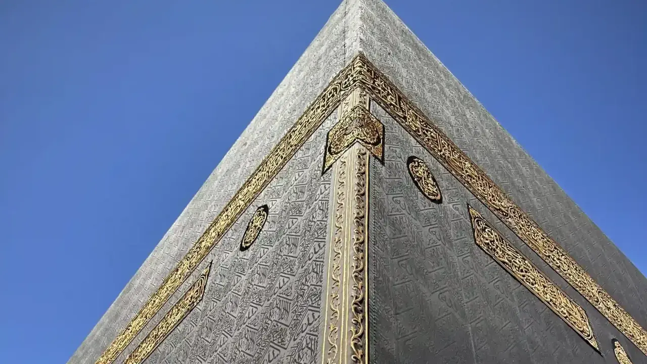 Die Kaaba in Mekka, Saudi-Arabien, mit ihrer schwarzen Hülle und goldenen Verzierungen vor blauem Himmel.