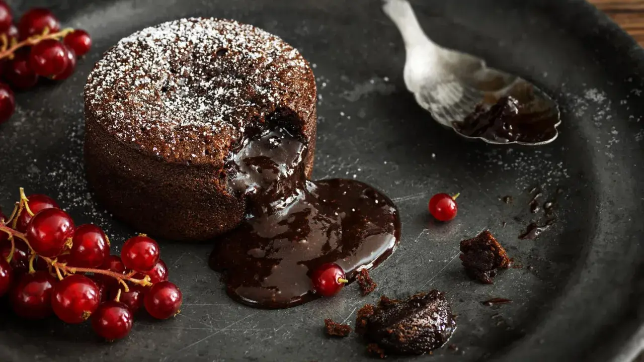 Schokoladen-Lava-Kuchen mit flüssigem Kern, bestäubt mit Puderzucker, garniert mit roten Johannisbeeren. Ein köstliches Lava Cake Rezept.