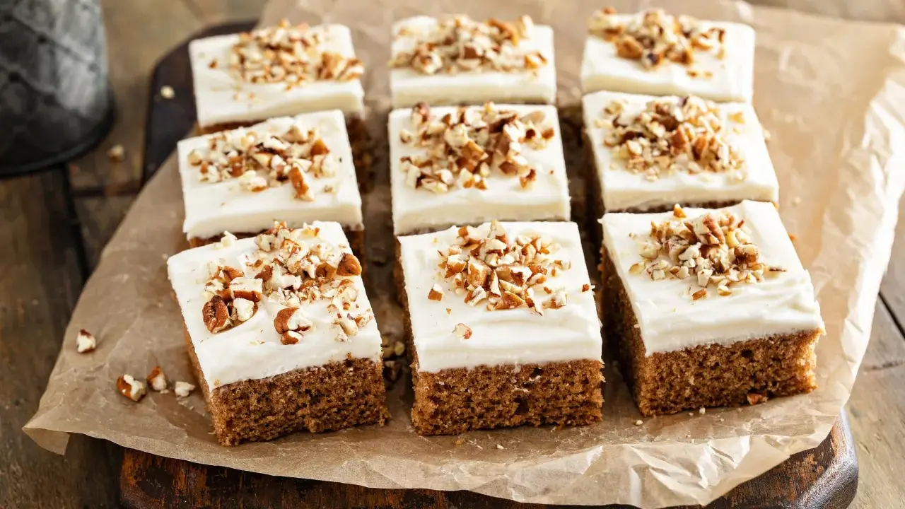 Nio bitar saftig morotskaka i långpanna med krämig frosting och hackade nötter, redo att avnjutas.