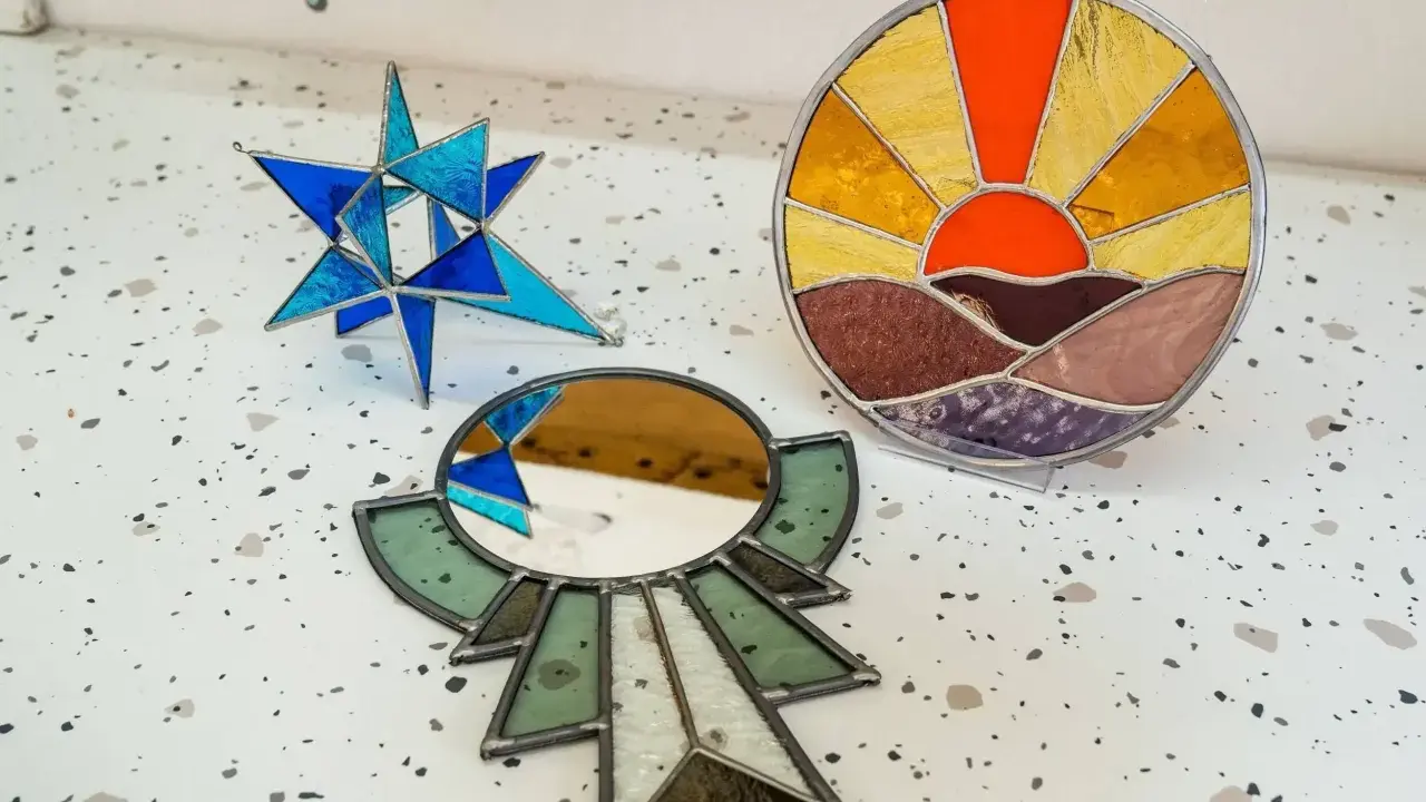 Trois pièces d'art en vitrail : une étoile bleue, un soleil couchant et un miroir ornemental. Créations d'un atelier vitrail Paris.