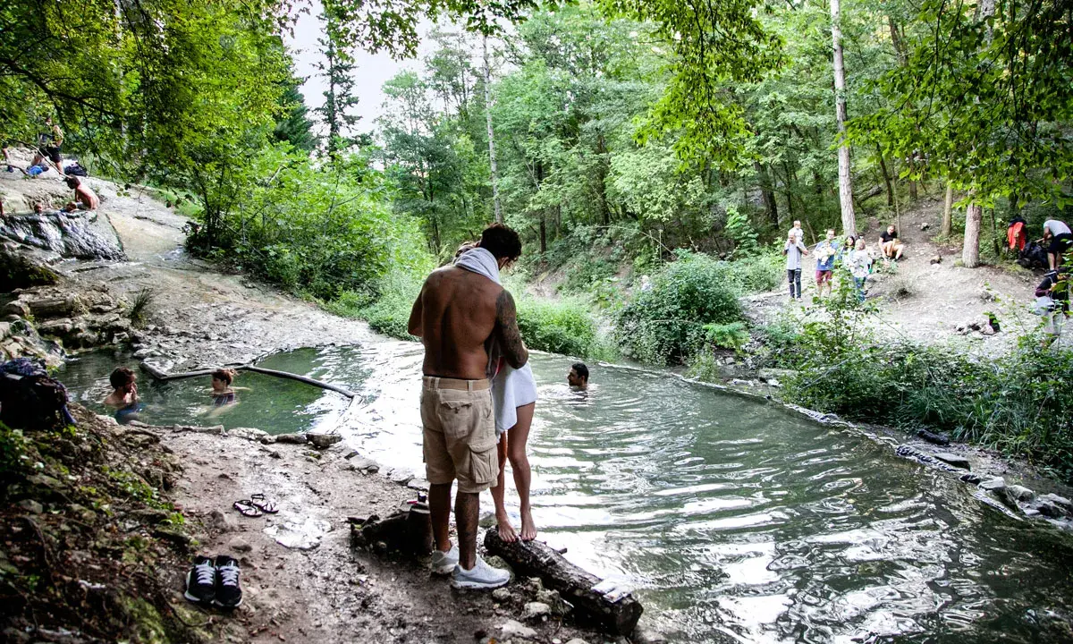 Persone si rilassano nelle acque termali dei Bagni di San Filippo, immersi nel verde di un bosco.