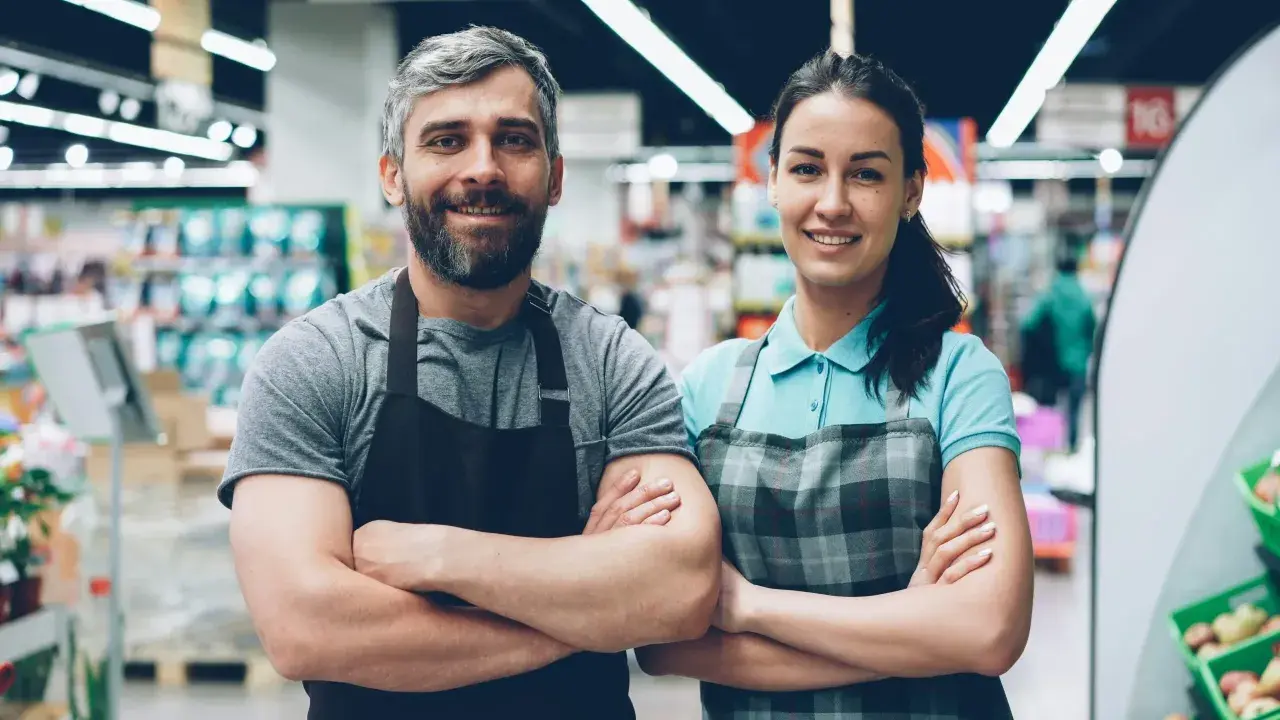 Deux employés souriants, habitués à rester debout toute la journée, posent dans un supermarché.