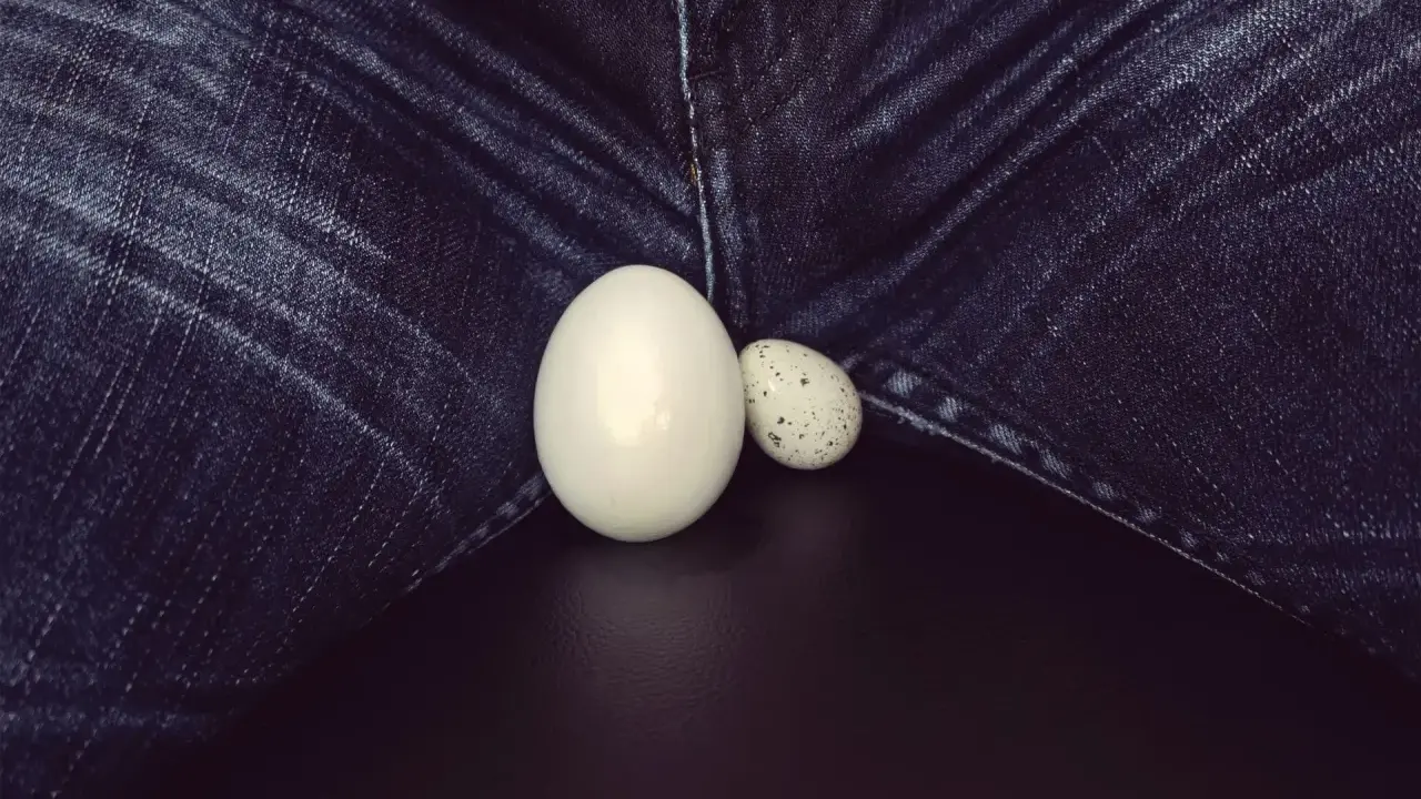 Dwa jajka, jedno duże, drugie małe, leżą na tle dżinsów. Powiększone jądro, symbol płodności.