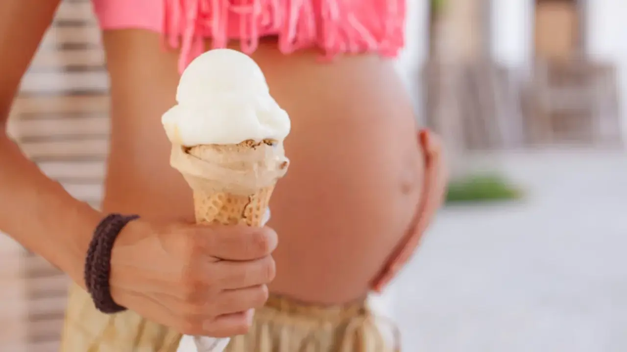 Schwanger und Lust auf Eis? Eine Frau hält eine Eistüte, während sie ihren Bauch streichelt.