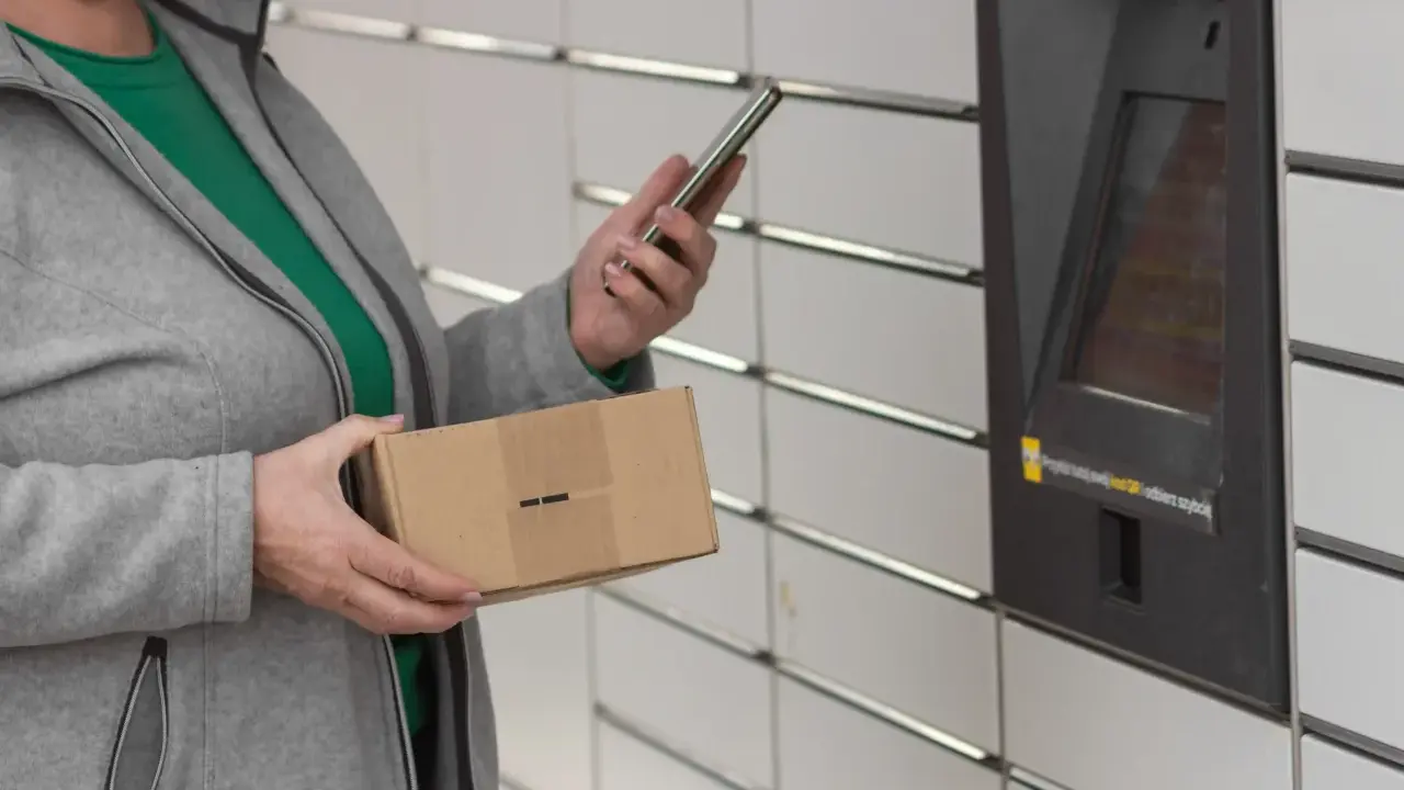 Kobieta z telefonem i paczką InPost przy automacie. Weryfikacja paczki InPost przebiega sprawnie.