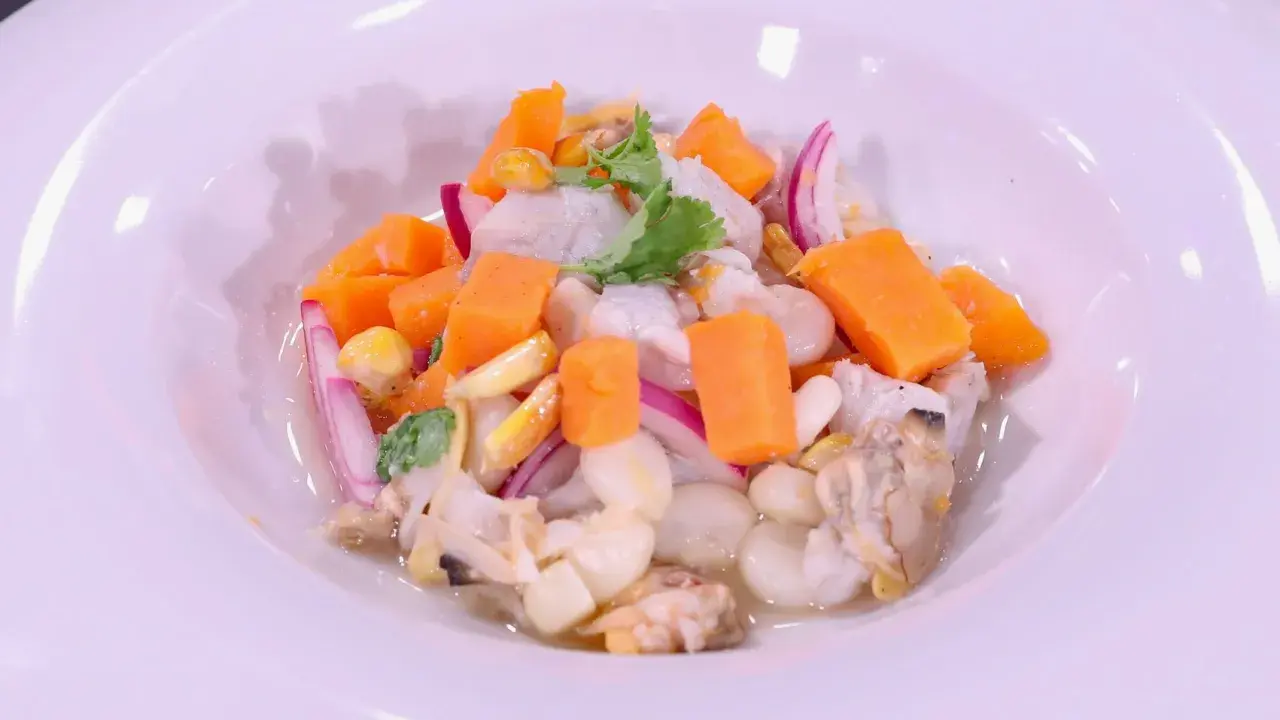 Delicioso ceviche de corvina con trozos de camote, choclo, cebolla roja y culantro, servido en un plato blanco.