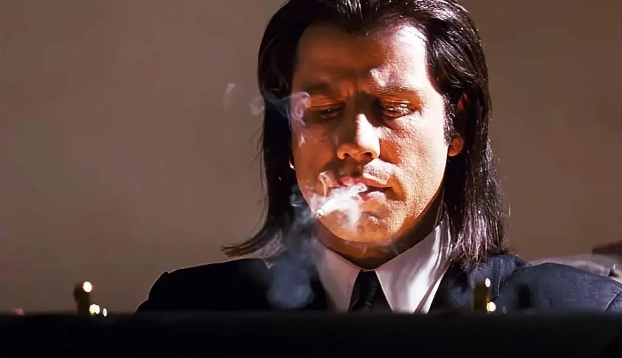 John Travolta i en ikonisk scen från filmer, med rök som virvlar runt hans ansikte.