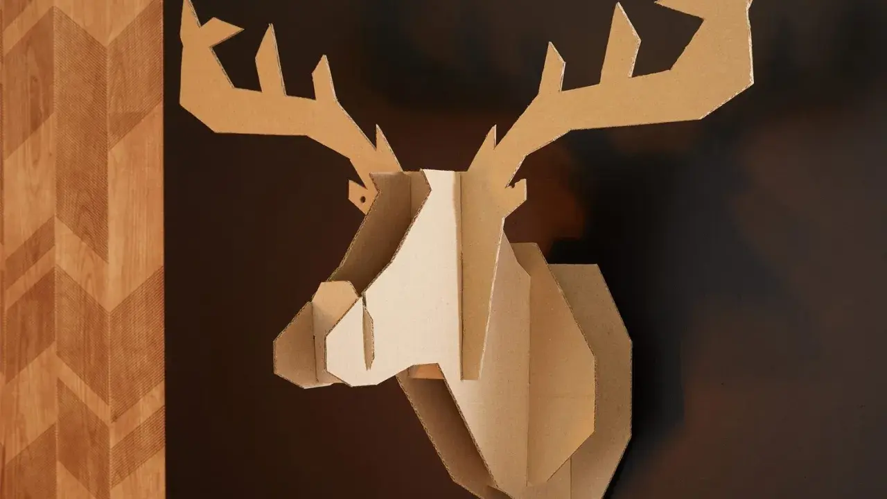 Trophée de cerf stylisé, œuvre de bricolage avec du carton de récupération, accroché sur un mur sombre à côté d'un panneau décoratif en bois.