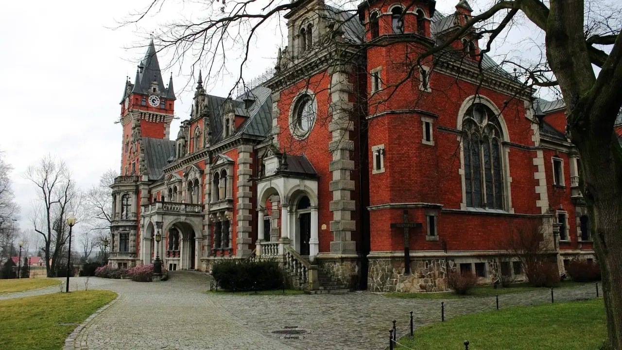 Pławniowice atrakcje: okazały pałac z czerwoną cegłą, wieżą zegarową i brukowanym dziedzińcem.