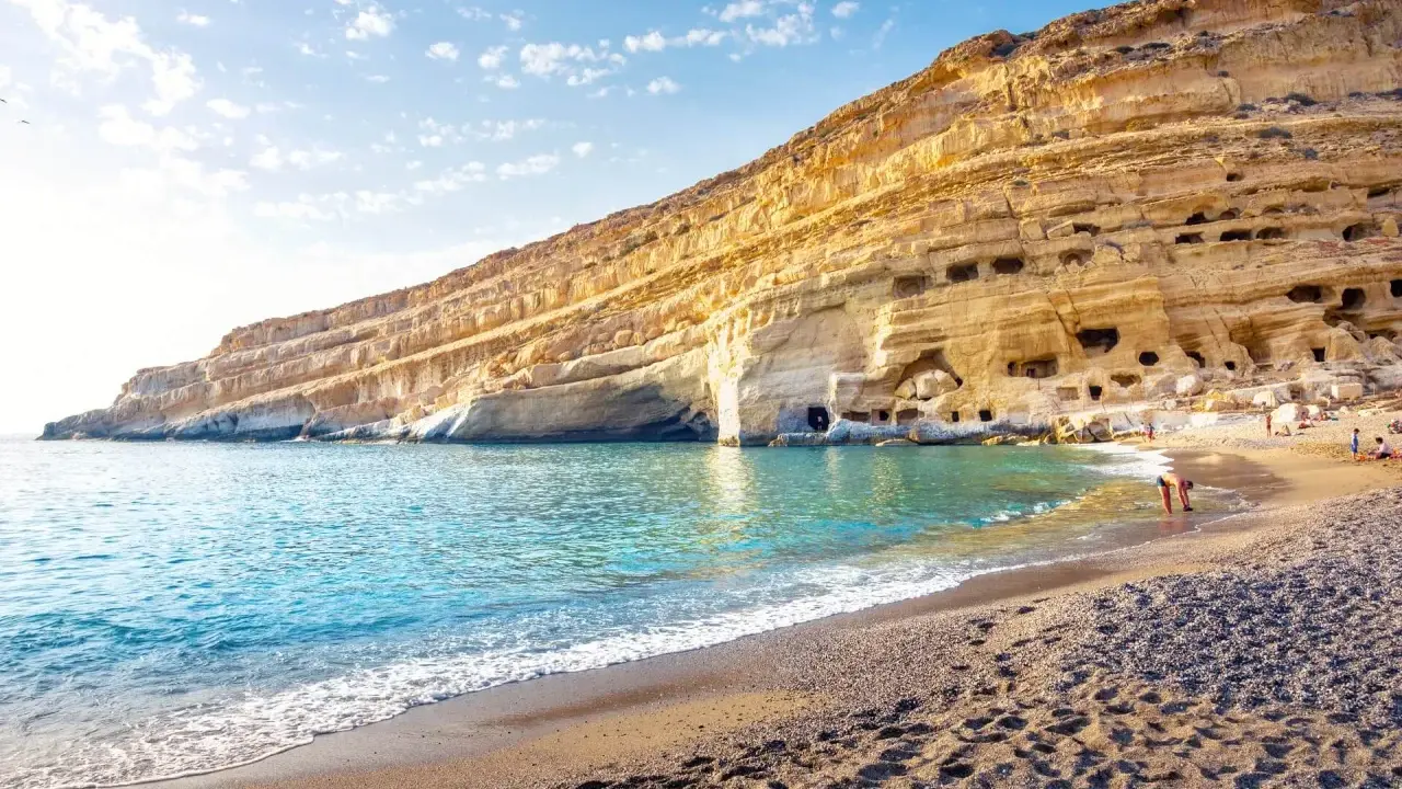 Ein malerischer Strand auf Kreta mit türkisfarbenem Wasser, das sanft an den Kiesstrand schwappt. Die beeindruckende Felswand mit ihren Höhlen bietet eine einzigartige Kulisse.