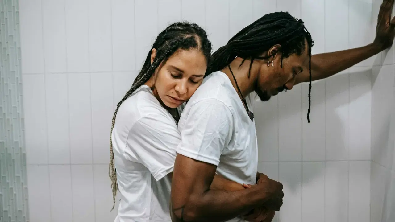 Una pareja se abraza con tristeza, reflejando el momento en que empiezan los problemas de pareja. Él se apoya en la pared, ella recuesta su cabeza en su hombro.