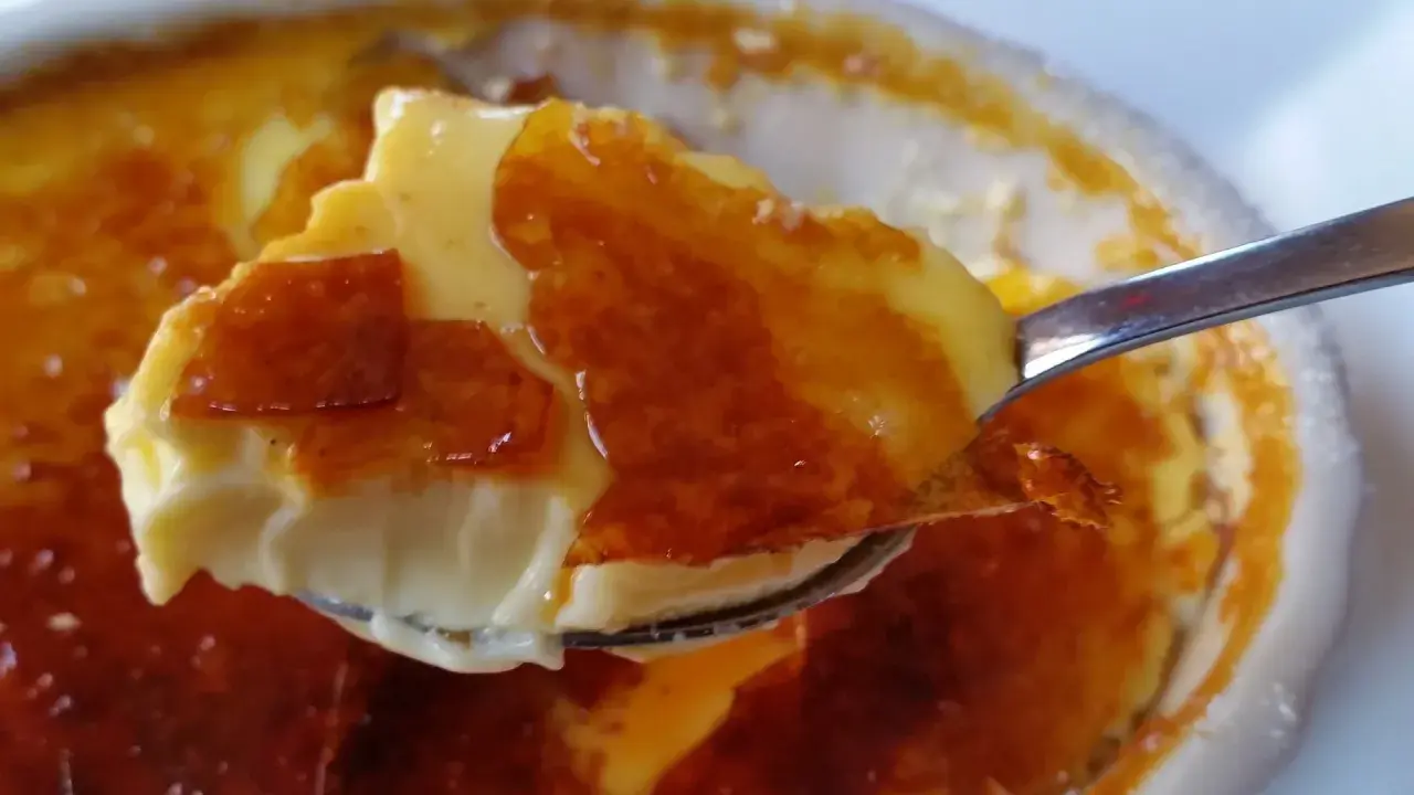 En sked lyfter en bit krämig creme brulee med knäckig karamelliserad yta.