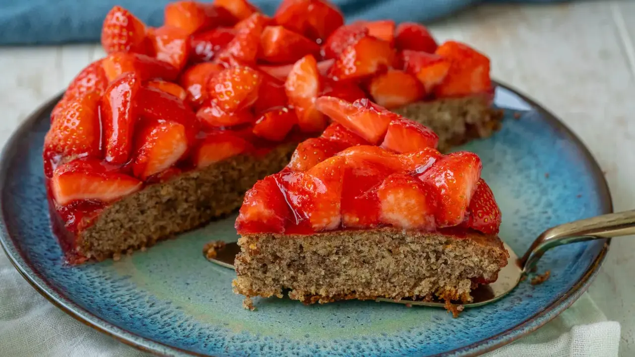 Ein saftiger, glutenfreier Erdbeerkuchen mit frischen Erdbeeren und glänzender Tortenglasur auf einem blauen Teller.