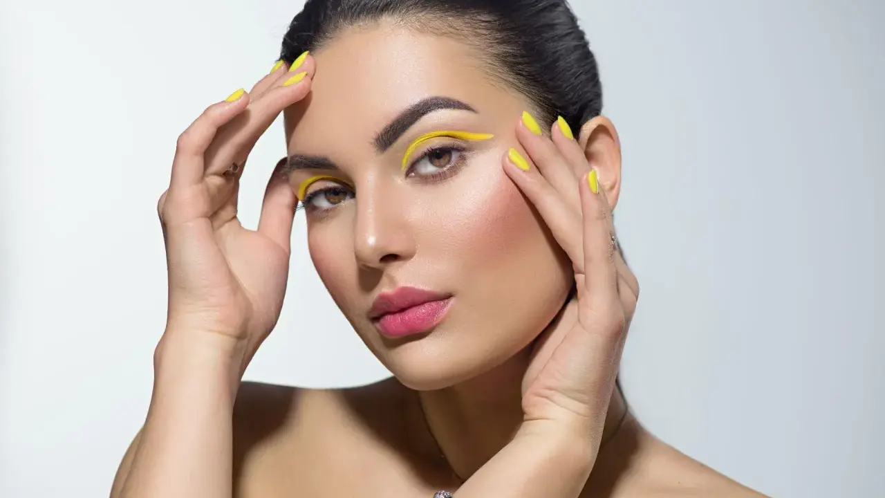 Mujer con un atrevido doble eyeliner amarillo y uñas a juego.