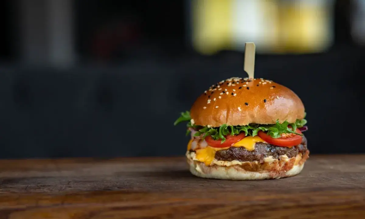 Apetyczny hamburger z serem, pomidorami i sałatą na drewnianym blacie.
