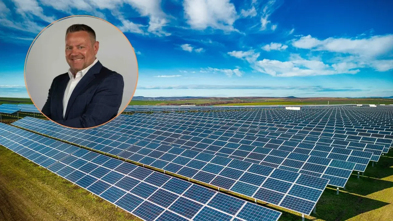 Uśmiechnięty mężczyzna w garniturze na tle farmy fotowoltaicznej. Obraz symbolizuje produkcję energii z fotowoltaiki w poszczególnych miesiącach.