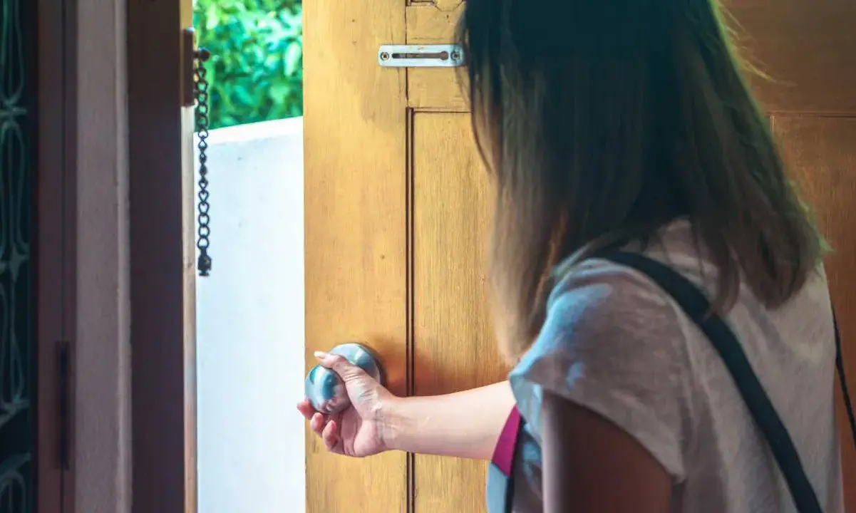 Mano che apre una porta, esitante, con l'ansia di uscire di casa che si fa sentire.