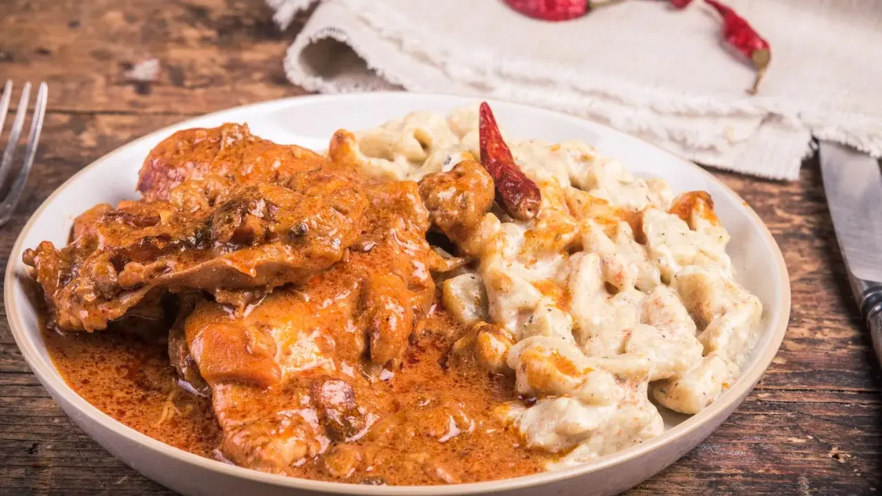 Gulasz z warzywami, podany z kremowym sosem i ozdobiony suszonymi papryczkami chili, kusi apetycznym wyglądem.