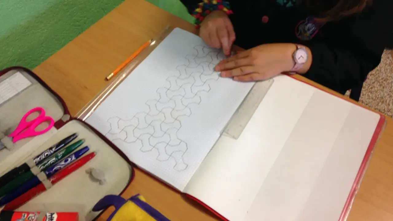 Bambina disegna un motivo geometrico su un quaderno di matematica. Matite, forbici e righello a portata di mano.