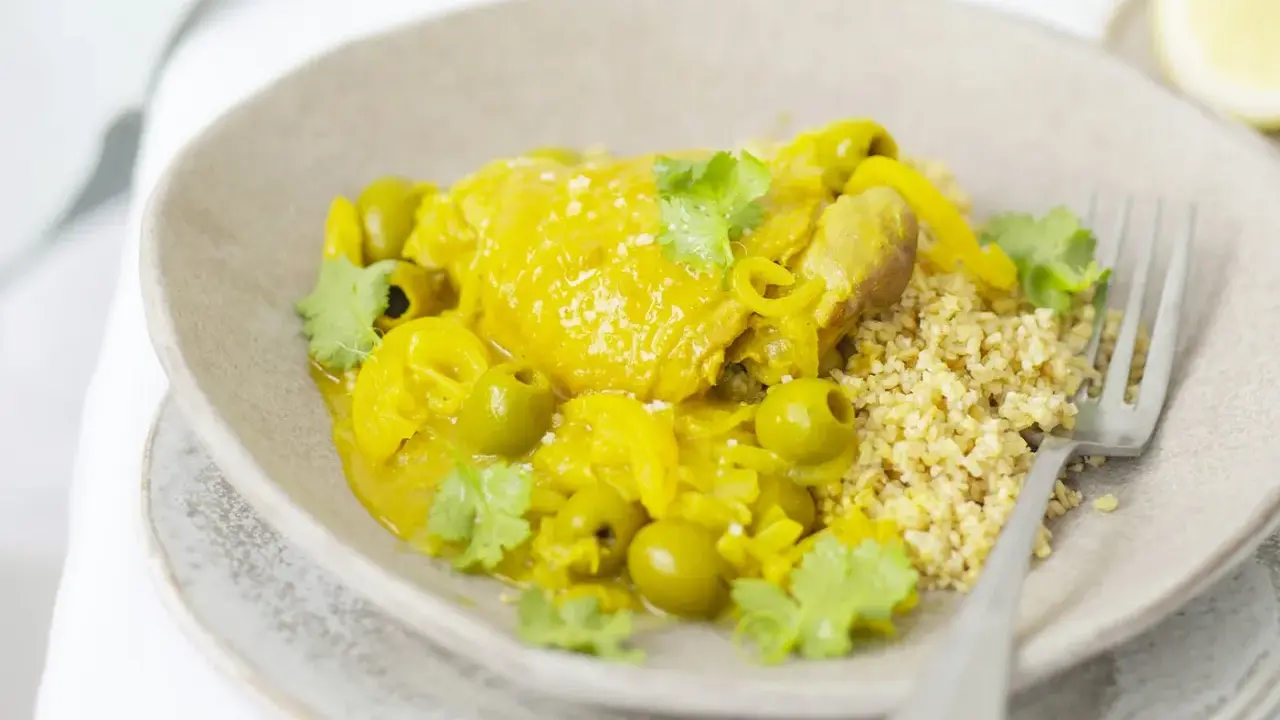 Un plat de tajine poulet citron, parfumé et coloré, servi avec du couscous et des olives vertes.