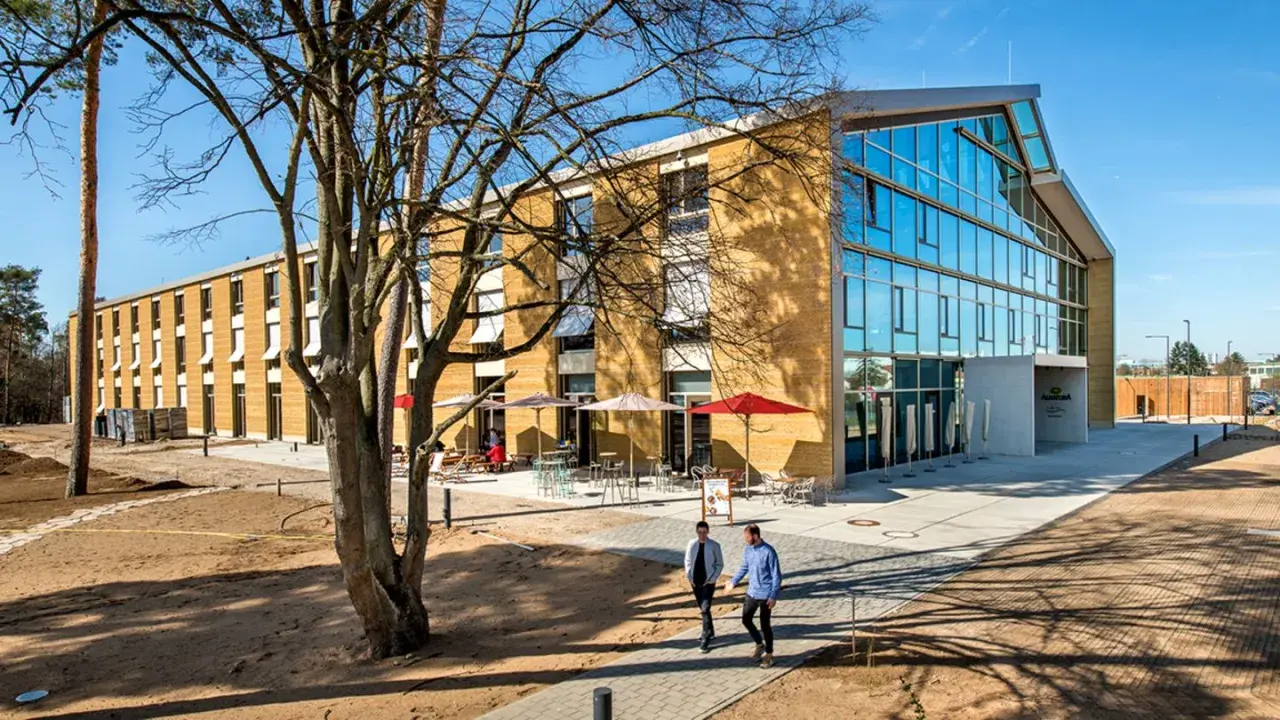 Modernes Gebäude mit Glasfront und Fassade aus nachhaltigen Materialien. Zwei Männer gehen auf einem Weg.