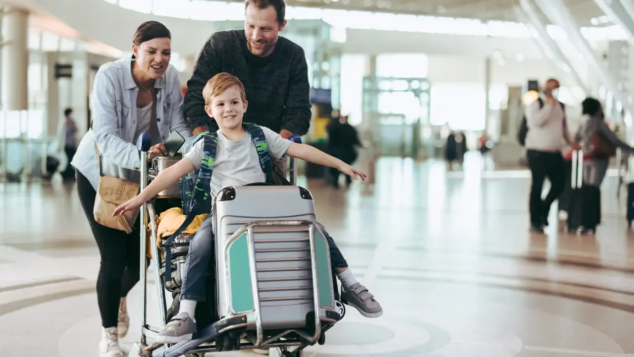 Familj på flygplatsen med ett barn sittandes på handbagage. De är glada och redo för sin resa.