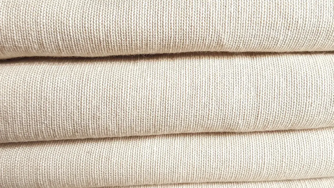 A stack of folded, natural-colored linen fabric. This image showcases the texture of linen, confirming that is linen a natural fiber.