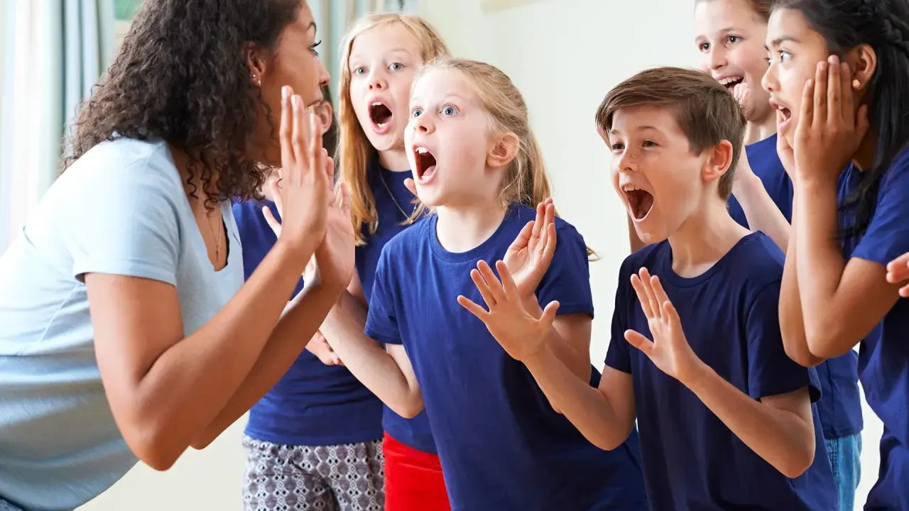 Bambini entusiasti in cerchio, con la maestra che guida attività di psicomotricità e linguaggio, stimolando espressioni vocali e corporee.