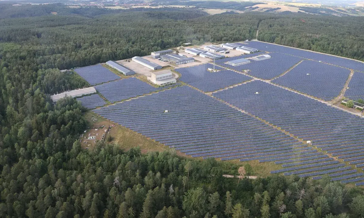Große Solaranlage im Wald, die Sonnenenergie sammelt. Gebäude und Reihen von Solarmodulen erstrecken sich über die Landschaft.