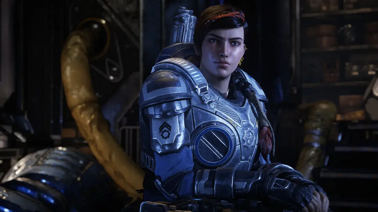 Kait Diaz w zbroi z Gears of War 5, z warkoczem i czerwoną opaską na włosach, w tle industrialne otoczenie.